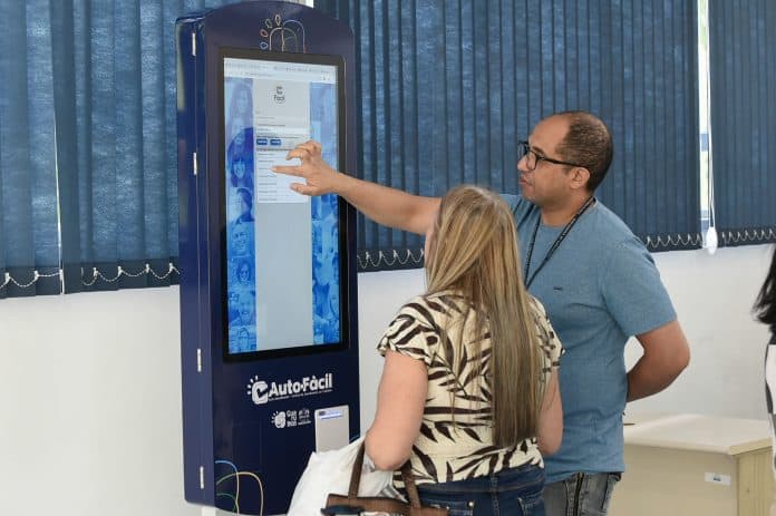 otem de autoatendimento AutoFácil de cor azul e branca instalado dentro da unidade do Fácil Bom Clima em Guarulhos. Uma pessoa utiliza a tela touch do equipamento para emitir documentos.