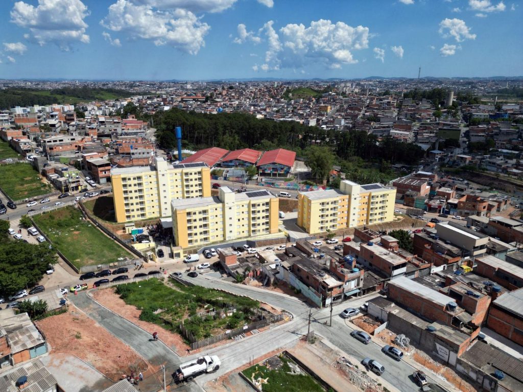 Fachada dos prédios da CDHU no Sítio São Francisco, em Guarulhos, apresentando sinais de abandono, mato alto e infiltrações após três meses da entrega simbólica.