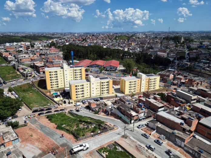 Fachada dos prédios da CDHU no Sítio São Francisco, em Guarulhos, apresentando sinais de abandono, mato alto e infiltrações após três meses da entrega simbólica.